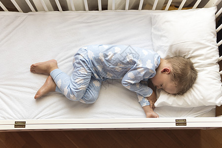 顶视图 可爱的小 23 岁学龄前男婴孩子在午餐休息时间穿着蓝色睡衣在家里用枕头甜甜地睡在白色婴儿床里 童年 休闲 舒适 医药 健图片