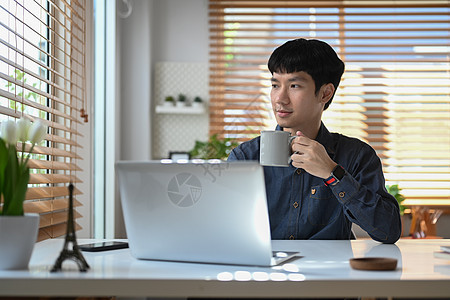 有思想的年轻商务人士喝咖啡 透过窗户看 早上在他的家庭办公室度过空闲时间图片