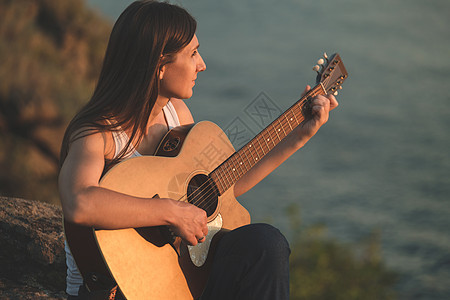 一个美丽的女人坐在岩石上弹原声吉他 漂亮的女孩在吉他上练习音乐 演奏和弦的女性吉他手图片