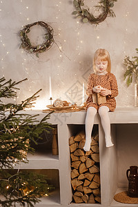 一位女孩在圣诞节前夕 在一个为新年节日装饰的美丽房子里玩 斯堪的纳维亚风格的内地有活林木和木楼梯裙子孩子圣诞礼物硬木工艺客厅脚步图片