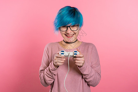 蓝色发型的漂亮女孩在Tv玩视频刺激游戏 在粉红色工作室墙上挂着摇棍 使用现代技术喜悦女士朋友们安慰玩家闲暇键盘电脑享受女性图片