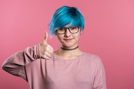 蓝头发的小朋克异性女人 在粉红背景上做拇指标记 笑着看镜头图片