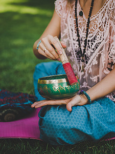 夏天 女人坐在绿色公园的瑜伽垫上玩唱歌碗 复古色调 美丽的女孩与 mala 珠子在绿草上打坐医疗保健女士乐器谐波瑜伽公园音乐康复图片