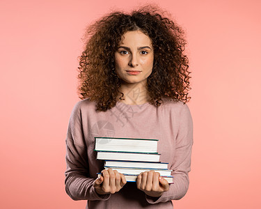 工作室的有粉红色背景的欧洲学生持有图书馆提供的大学书籍 妇女很高兴毕业 在业者中阅读快乐学校微笑笔记本青少年爱好教育黑发女孩图片