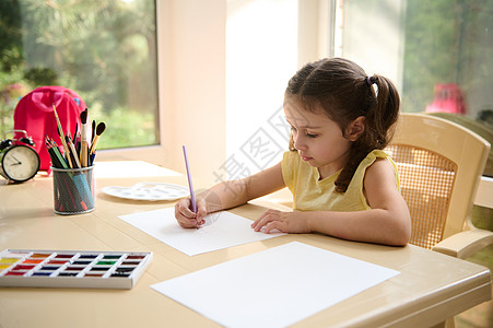 美丽的女学生放学后享受艺术课 坐在桌子上 在白纸纸页上画画照片背景图片