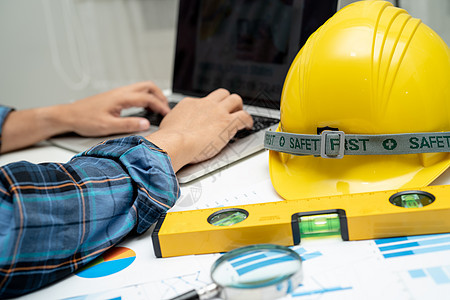 具有建筑房屋计划项目蓝图 图表和黄色头盔以及工程施工工具的亚洲工程师设计师绘画安全帽帽子统治者安全办公室建设者工人桌子图片