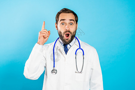 留着胡子的年轻思考思考医生的肖像有想法时刻在蓝色工作室背景上竖起手指 微笑快乐的医生显示尤里卡手势图片