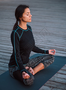 专注的黑衣女孩在木制海滨练习瑜伽冥想 莲花姿势的女人 伸展 练习 健康的生活方式理念 复制空间运动身体成人数字女性训练宠物福利头图片