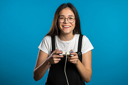 漂亮的亚洲女孩在Tv上玩电动刺激游戏 在蓝色工作室墙上用摇摆棍 使用现代技术按钮女性乐趣控制电脑娱乐沙发女士视频玩家图片