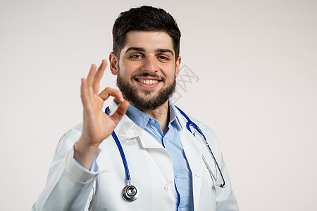 医生在白色背景上签了名 穿着医疗大衣的年轻阳性男子微笑着相机 胜利者 成功者 身体语言图片