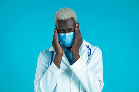 身穿专业医疗白大衣的年轻非洲医生头痛 工作室肖像 把手放在头上的家伙 在蓝色背景下被隔离 问题 医学 疾病的概念图片