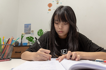 亚裔女学生在书桌上写家庭作业和阅读书知识分子家庭作业童年测试学校桌子笔记本蜡笔绘画女孩图片