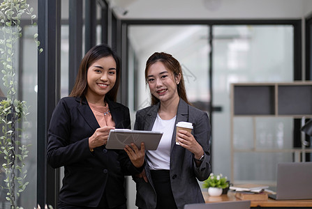 两名美丽的亚洲女商务人士利用数字平板电脑咨询和分析办公室工作的信息站立起来 她们站在办公室工作微笑桌子人士员工商业女性技术职员商图片