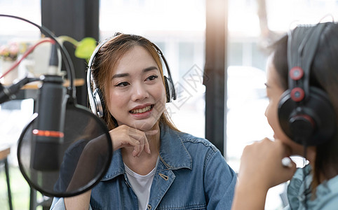 微笑着两个亚洲年轻女性 男性电台主持人戴着耳机 在谈话时使用麦克风 谈话 在演播室的广播中一起录制播客 制作录音音频概念的技术音图片