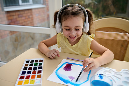 快乐的孩子 可爱可爱的欧洲学龄前小女孩 在耳机里听音乐 学习水彩绘画图片
