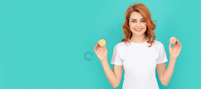 快乐的女士在蓝背景上拿着甜美的马卡龙法国饼干 女性孤立的脸像 标语和模拟复制空间图片