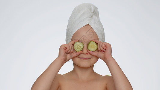 手持黄瓜 遮眼 天然化妆品 面部皮肤护理的微笑女女童图片