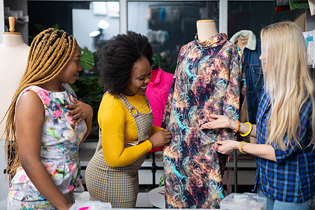 两个深肤色的顾客在裁缝店里看裙子长发织物人体服装检查设计师服装设计师微笑店铺节目图片