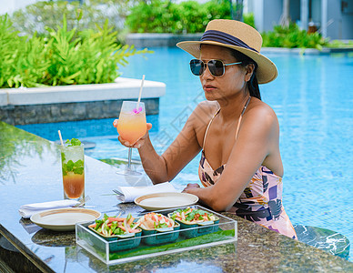 戴帽子和鸡尾酒的亚裔女性在游泳池 横旗度假概念中放松比基尼晒黑晴天旅游天堂酒店海洋横幅食物奢华图片