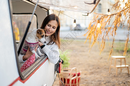 白种女人向车窗外看 拥抱她的狗杰克罗素泰瑞尔 在秋天搭露营冒险窗户享受小狗远足者房子快乐假期旅行房车图片