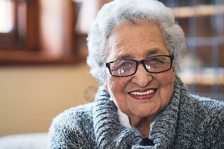 在家坐在沙发上笑着享受退休快乐的长得像肖像般美丽的老年妇女图书幸福个性头发灰色女士眼镜知识皱纹长椅图片