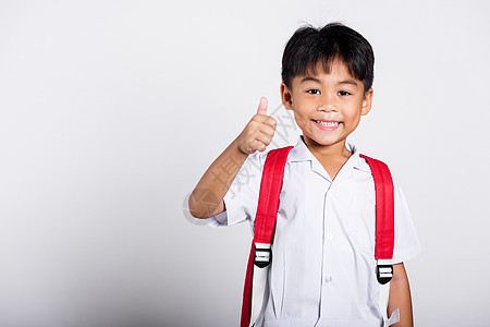 亚洲可爱的小孩 笑着快乐 穿着学生泰文校服 红裤子展示大拇指举起手指男生眼镜喜悦教育乐趣孩子微笑幼儿园背包童年图片