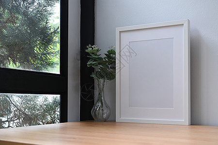 白色照片框和在窗户附近的木制桌子上的陶瓷工厂图片
