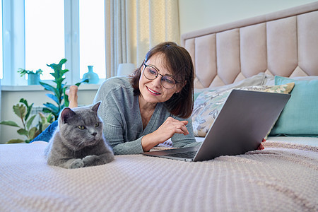 女人和猫一起躺在家中的床上 女性使用笔记本电脑互联网沙发房子自由职业者头发工作快乐小猫动物成人图片