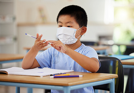 男孩在课堂上做功课 在小学课桌上写作和数数时 带着面罩进行教育 covid 和学习 亚洲儿童佩戴防护装置以阻止病毒传播图片