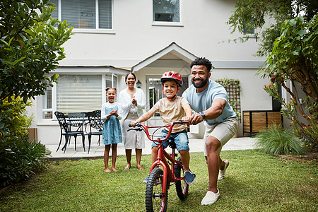 儿童骑车出去玩骑自行车的男孩在户外自家花园里与自豪的爸爸和幸福的家庭一起学习 微笑的父亲教有趣的技能 帮助和支持他兴奋的小儿子骑车 骑自行车和背景