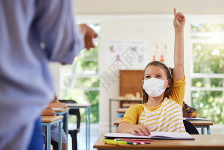 戴着 covid 面罩的聪明学生在教室或小学向老师询问有关电晕病毒流行的问题 小女孩举手在课堂上回答与医疗保健相关的话题图片