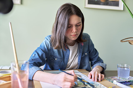 女孩坐在桌边的家里 画着水彩色的少女绘画图片