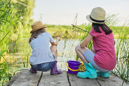 女孩坐在木码头上 在桶里抓水蜗牛池塘闲暇朋友码头游戏孩子们假期享受孩子幸福图片