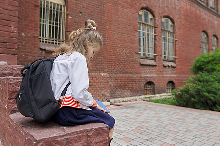 在学校院子里坐着背背包的女童阅读笔记本 复制空间教育建筑小学生学习者成功女性孩子优胜者学习青年图片