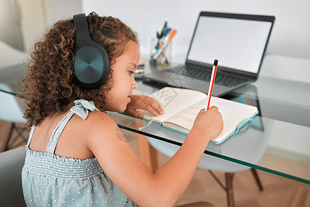一个聪明聪明的小女孩使用笔记本电脑和耳机参加在线或虚拟课程的家庭教育 在家听音乐写作 工作或做家庭作业的幼儿图片