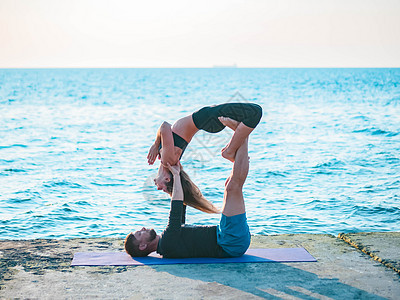 年轻美丽的夫妇在靠近水的海滩上练习杂技瑜伽 男人和女人在自然背景下做日常户外练习 健康的生活方式概念天空姿势伙伴女士活力灵活性成图片