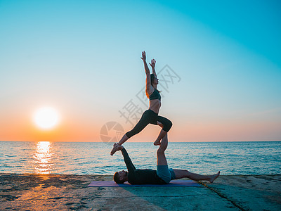 在海边做Acroyoga的年轻夫妇 男人躺在混凝土板上 让女人靠在脚上平衡 漂亮的一对一起练瑜伽海洋灵活性运动身体杂技姿势女性女图片