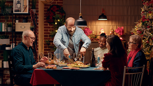 光荣的丈夫在享受圣诞晚宴的同时 为客人切烤鸡肉图片