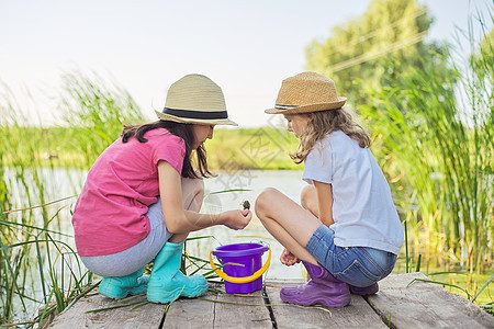 女孩坐在木码头上 在桶里抓水蜗牛孩子们朋友友谊木头童年乐趣假期闲暇活动享受图片