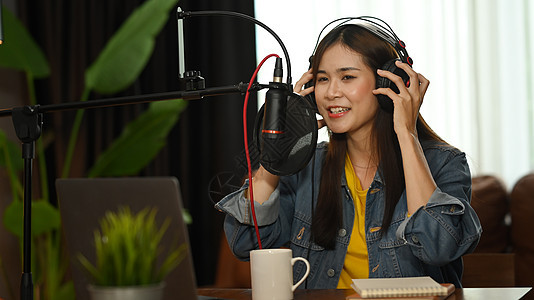 亚洲女性播客戴着耳机在家庭工作室录制播客 广播 播客 博客和技术概念工具职业收音机嗓音女士桌子记录说话麦克风娱乐图片