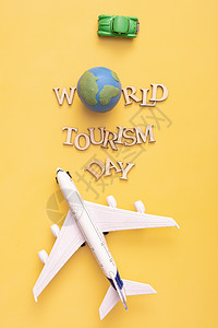 世界旅游日文字来自黄色背景的地球仪 汽车和飞机的木制字母 顶视图 平躺图片