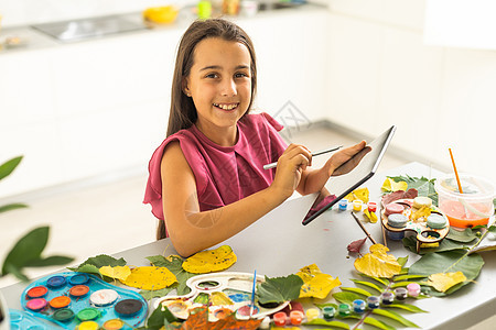 小女孩在家中涂上刷子和秋天艺术的颜料木头桌子落叶头发儿童爱好叶子绘画水彩女孩图片