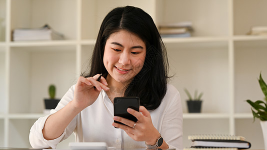 微笑的亚洲女上班族打短信 在手机上在线聊天金融帐户企业家冲浪电脑阅读网络顾问会计报告图片