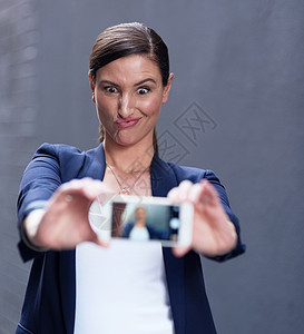 连CEO也有愚蠢的一面 一个快乐的女商务人士 用她的智能手机来玩自拍图片