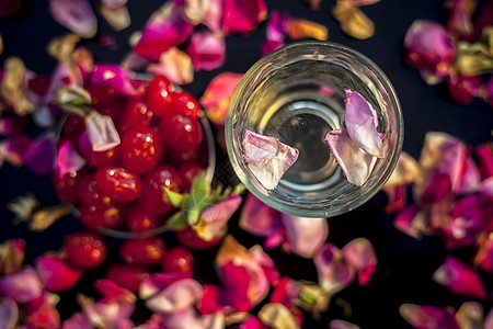 由一些与水充分混合的甜樱桃组成的黑色表面上自然发光皮肤的面膜 拍摄新鲜樱桃 一杯水和一些展开的玫瑰花瓣保湿身体玻璃润肤木板护理温图片