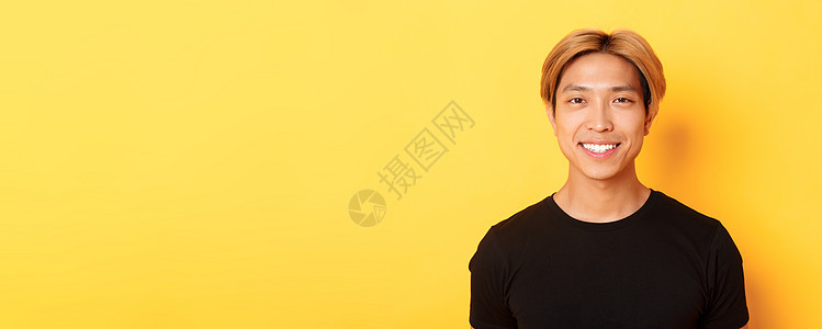 身穿黑色 T 恤的金发亚洲帅哥的特写 对着镜头笑得很开心 站在黄色背景上发型情感男性广告成人促销快乐男朋友理发头发图片
