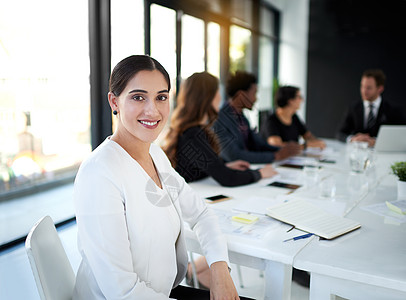 我们的成功策略都已到位 一位女商务人士坐在会议室与背景中的同事开会的肖像图片