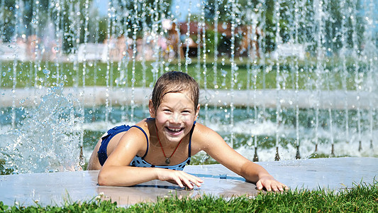 快乐的八岁穿泳衣的女孩在街头城市喷泉 户外 公园 夏日 阳光炎热的假期中玩得开心喜悦幸福闲暇活动享受行动假期家庭软管飞溅图片