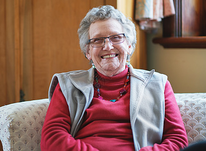 快乐的年长妇女坐在沙发上微笑 在家享受退休生活红色头发知识祖母长椅女士学习图书馆眼镜书架图片
