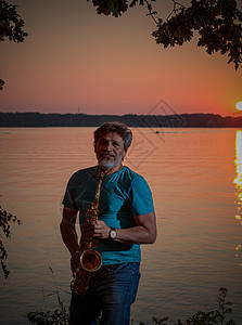 一个成年男子在日落时 晚上在河边玩萨克斯海滩金子闲暇蓝色男性旋律橙色娱乐乐器音乐图片